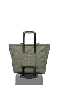 Sac fourre-tout matelassé vert avec un motif texturé ; il possède des poignées robustes et une poche à glissière, attaché à une valise à roulettes grise.