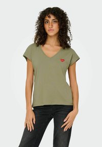 Oliven grøn V-hals T-shirt lavet af blødt stof, med korte ærmer og et lille rødt hjerte designet på venstre brystområde.