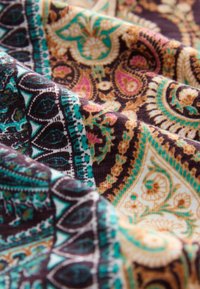 Vzorovaná látka v bohaté hnědé, tyrkysové a zlaté barvě. Obsahuje složité designy paisley a květinové motivy s jemným, strukturovaným povrchem.
