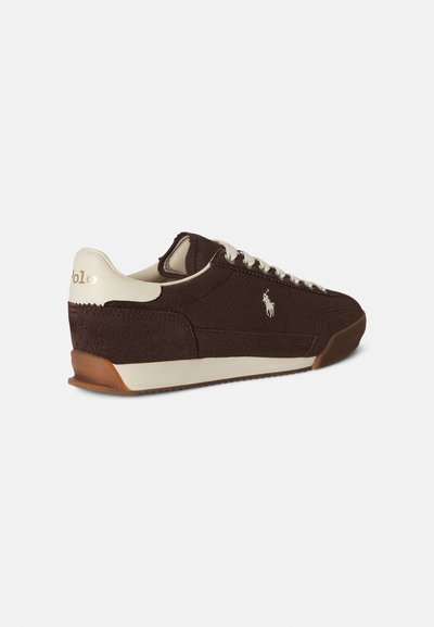 Καφέ σουέντ αθλητικό παπούτσι με ανοιχτό μπεζ λεπτομέρειες, υφή στην επάνω επιφάνεια, λευκά κορδόνια και εξωτερική σόλα από καουτσούκ σε φυσικό χρώμα. Διαθέτει λογότυπο στο πλάι.