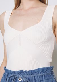 Body cremoso a coste con scollatura a V e pannello testurizzato diagonale. Caratterizzato da spalline larghe e abbinato a una gonna di jeans.