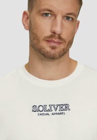 Biała bawełniana koszulka z haftowanym w granatowym kolorze logo "S.OLIVER CASUAL APPAREL", okrągły dekolt, krótkie rękawy i gładka tekstura.