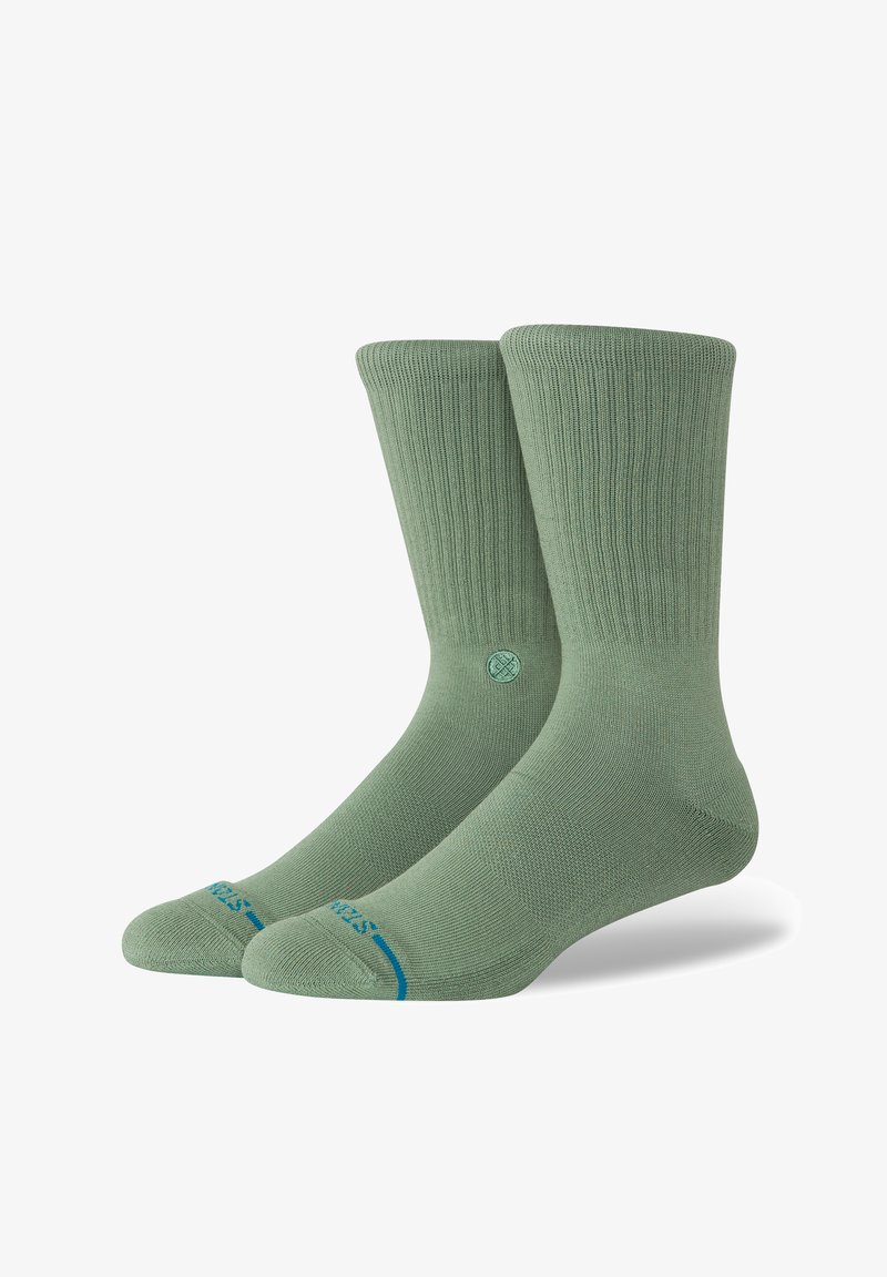Groene crew-sokken van ribstof, met een blauwe accent bij de teen en een rond logo bij de enkel. Gladde textuur.