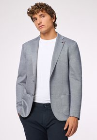 Blazer grigio chiaro realizzato in tessuto testurizzato, dotato di chiusura a due bottoni, revers a puntale e tasche frontali. Abbinato a una t-shirt bianca.