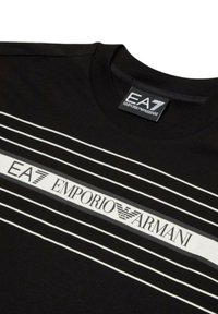 T-shirt nera con strisce bianche e logo "EA7 EMPORIO ARMANI" al centro. Collo rotondo, texture liscia, design casual.
