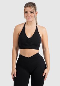 Zwarte haltercrop-top met een gerimpeld middenstuk, gemaakt van rekbare stof, gecombineerd met zwarte high-waisted leggings met een V-vormige tailleband.