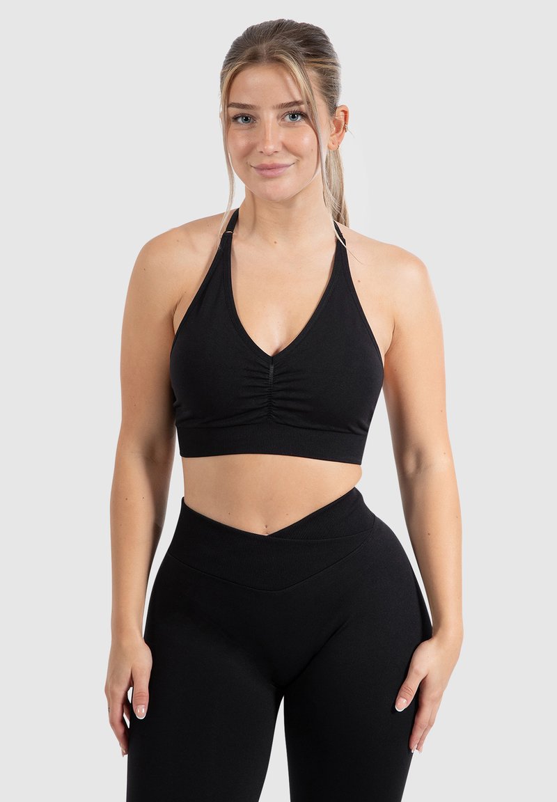 Zwarte haltercrop-top met een gerimpeld middenstuk, gemaakt van rekbare stof, gecombineerd met zwarte high-waisted leggings met een V-vormige tailleband.