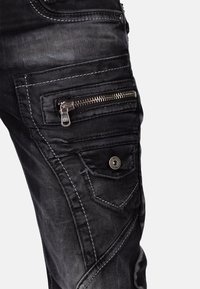 Zwarte denim broek met respectievelijk rits- en knoopzakken, contrasterende stiksels en een gemêleerd uiterlijk. Opvallend door de gedetailleerde panelen.