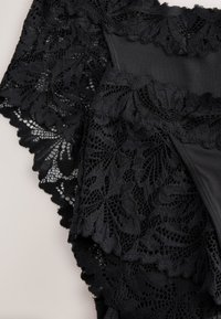 Schwarze Spitzen-Damenunterwäsche mit Blumenmustern und gezackten Rändern auf hellem, einfarbigem Hintergrund.