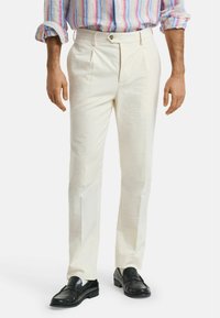 Hvide plisserede bukser med et struktureret stofdesign og en lige pasform, parret med sorte loafers, viser en neutral farvepalet.