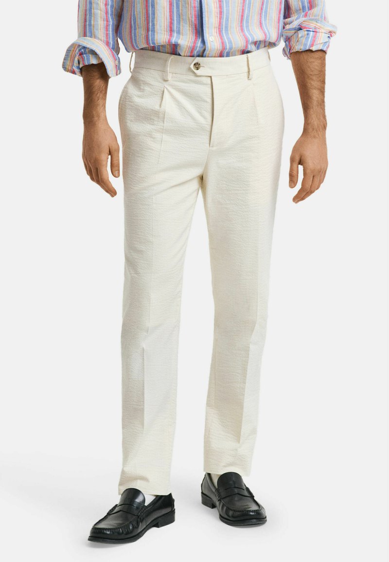 Hvide plisserede bukser med et struktureret stofdesign og en lige pasform, parret med sorte loafers, viser en neutral farvepalet.