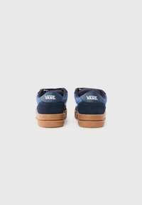 Navy blue suede sneakers with gum rubber soles, featuring a padded collar and a logo patch on the heel. Rounded toe and low-top design.