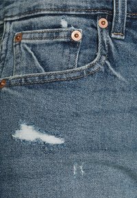 Jeans de denim azul claro con un diseño desgastado, áreas deshilachadas, remaches de color cobre y un estilo clásico de cinco bolsillos.