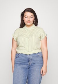 Camisa de manga corta abotonada en rayas verticales de color verde claro y blanco, con cuello y mangas enrolladas, combinada con jeans azules.
