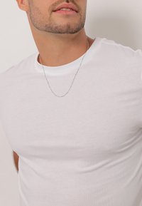 Tricou alb cu mânecă scurtă, realizat dintr-un material moale și neted. Are un colier subțire din lanț argintiu, cu detalii de mici mărgele.