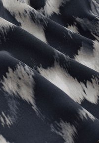 Dark fabric with abstract white and gray brushstroke patterns creating a soft, flowing texture with visible folds.