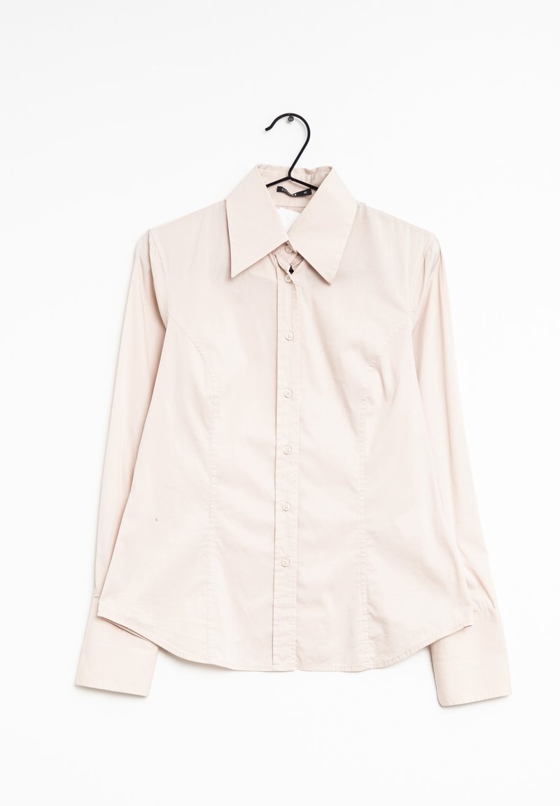 Chemise beige clair à manches longues avec col large, suspendue sur un cintre noir sur fond blanc.