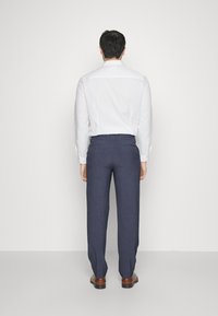 White long-sleeve shirt with buttoned cuffs, dark blue trousers in a smooth texture, and brown shoes. Viewed from the back, plain background.