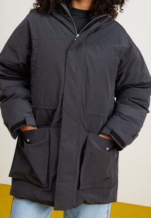 Zwarte, gevoerde parka jas met een rits aan de voorkant, grote voorzakken en een capuchon. Heeft een zachte textuur en een comfortabele pasvorm.