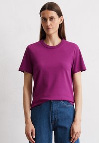Fuchsia T-shirt met korte mouwen, gemaakt van katoen, met een ronde halslijn en een relaxte pasvorm. G gedragen met blauwe denim jeans.