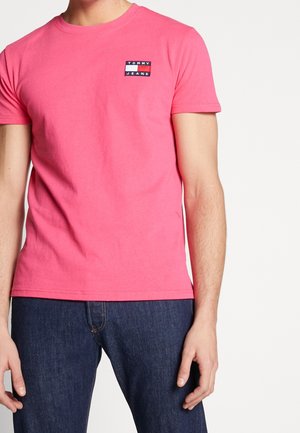 Roze katoenen T-shirt met een klein blauw, wit en rood geborduurd logoplaatje op de linkerborst; korte mouwen en een ronde hals.