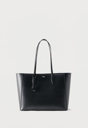 Schwarze Leder-Shopper-Tasche mit langen Trägern und kleinem goldenem "BOSS" Logo auf der Vorderseite, präsentiert vor einem schlichten, hellen Hintergrund.