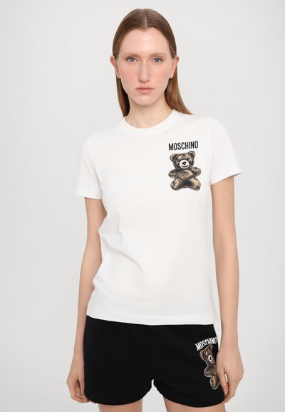 Camiseta blanca de cuello redondo con un gráfico de un oso pardo y el texto "MOSCHINO" en el lado izquierdo del pecho. Material de algodón, mangas cortas.