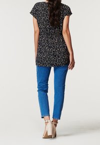 Marinblå blus med blommönster och korta ärmar, markerad midja, kombinerad med ljusblå jeans och beiga klackskor med blockklack. Slät tygtextur.