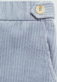 Țesătură de catifea cord cu dungi verticale, de culoare gri deschis, având un detaliu cu nasture la talie și un buzunar lateral. Textură moale și aspect cald.
