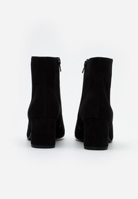 Bottines en daim noir avec un talon épais. Fermetures éclair latérales pour un enfilage facile. Texture lisse avec une finition mate et un design à bout rond.