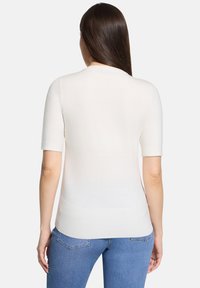 Haut à manches courtes beige clair en maille douce, à la coupe ajustée et avec une texture côtelée subtile, associé à un jean bleu.