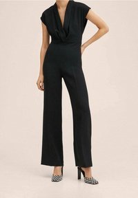 Zwarte jumpsuit met een gedrapeerde V-hals, korte mouwen en wijde pijpen. Gecombineerd met geruite hoge hakken. Soepele textuur.