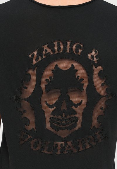 Crna majica s mrežastim premazom i izvezenim dizajnom lubanje. Tekst glasi "ZADIG & VOLTAIRE" u stiliziranom fontu.