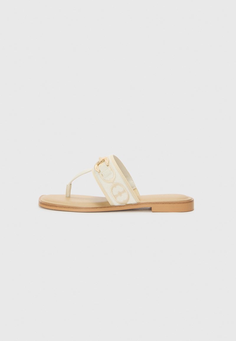 Tongs blanches avec une lanière texturée présentant un motif de logo, des éléments en métal doré et une semelle plate couleur tan.
