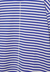 Modrý a biely látkový materiál s horizontálnymi pruhmi a stredovým zvislým švom, vykazujúci mierne vrásky a prehyby.