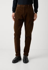Brune kordfløjsbukser med lige ben, som har en knaplukning og bæltestropper. Sat sammen med sorte loafers.