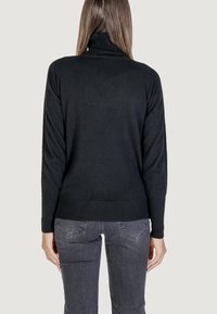 Pull à col roulé noir avec une texture lisse et un ourlet côtelé, doté de manches longues et d'un ajustement décontracté. Porté avec un jean gris.