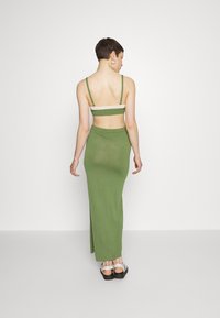 Conjunto verde de duas peças, apresentando um top ajustado com alças finas e uma saia longa e justa. O tecido tem uma textura suave e um design minimalista.