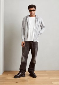 Gray zip-up hoodie with kangaroo pockets, white t-shirt underneath, black distressed jeans, and chunky black shoes, on a wooden floor.