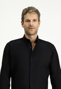 Camicia nera con colletto a punta. Presenta una texture liscia e maniche lunghe. I bottoni sono di un colore nero abbinato.