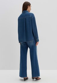 Camicia di denim e jeans a gamba larga di colore blu scuro. La camicia presenta un yoke posteriore e polsini con bottoni, mentre i jeans hanno una vestibilità dritta e un orlo sfilacciato.