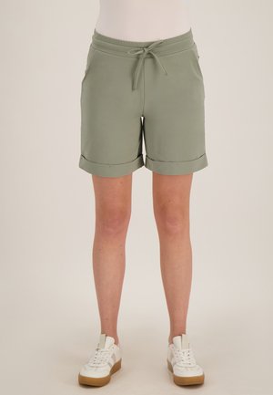Lichtgroene short met trekkoord en omslagen zoom, gedragen met witte sneakers door een persoon die voor een effen achtergrond staat.