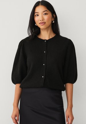 Zwarte gebreide cardigan met korte pofmouwen, ronde halslijn en vijf kleine knopen aan de voorkant. Zachte textuur, casual ontwerp.