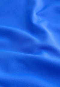 Hladká modrá látka s jemnými záhyby a jemnou diagonální texturou, vytvářející na povrchu jemné stíny a světla.