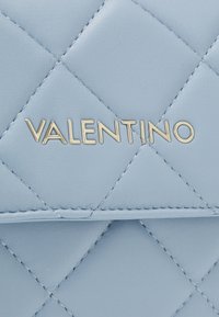 Ljusblå quiltad läderväska med det guldfärgade präglade varumärkesnamnet "VALENTINO" på framsidan. Detaljerad sömnad framhäver texturen.