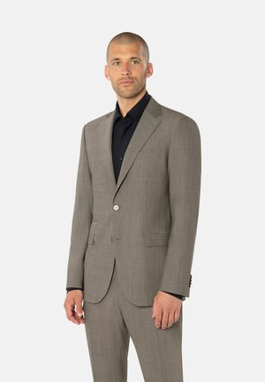 Lichtgrijs pak van gestructureerde stof, met een enkele knoopsluiting, notch revers en twee voorzakken, gedragen over een zwart shirt.