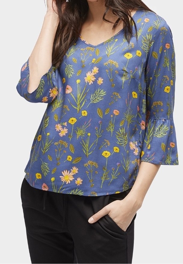 Blouse florale bleue à manches cloche, ornée de motifs floraux roses, jaunes et verts, confectionnée dans un tissu léger avec un col en V.