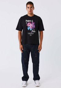 Camiseta negra con gráfico floral y texto superpuesto; combinada con jeans oscuros con patrones de estrellas y zapatillas deportivas blancas.