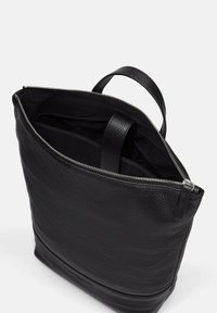 Sac en cuir noir avec une surface texturée, fermeture à glissière, et une seule poignée supérieure, offrant un intérieur spacieux.