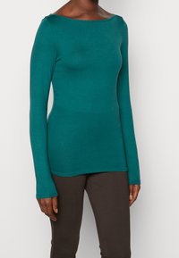 Teal långärmad topp med bred båtkrage, tillverkad av ett mjukt, lätt material. Har en figursydd silhuett och mjuk textur.